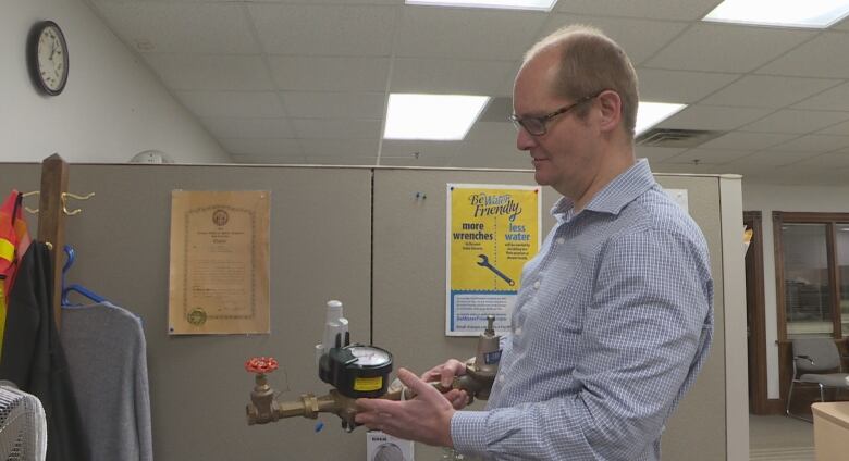 A man with glasses and a blue shirt holding a water meter