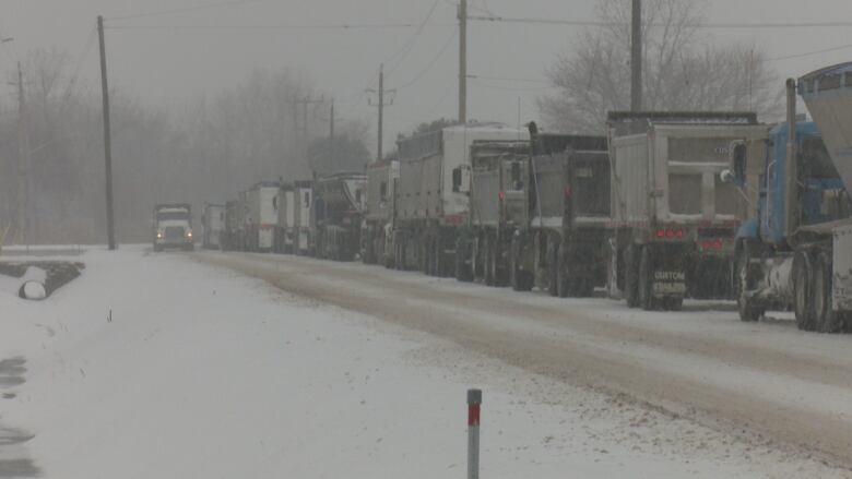 A line of trucks waits on the right side of the road. One truck in the distance drives up the left side of the road. The sky is hazy with precipitation.