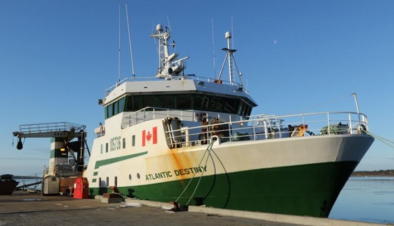 A large green and white trawling ship at dock.