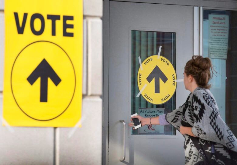 A woman opens a door with a sign that says VOTE with an arrow pointing inside