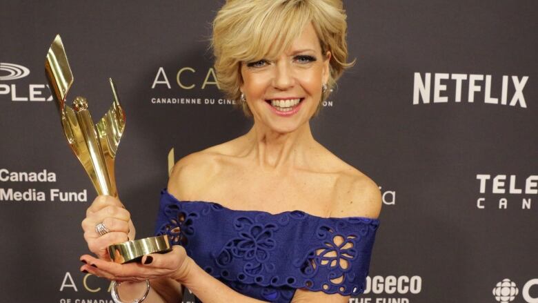 A woman in a blue gown holds up a golden trophy.