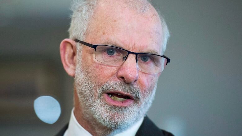 A closeup photo of a bald man with glasses and a beard.