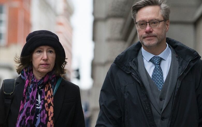 Parents of Jack Letts, Sally Lane and John Letts hold hands walking on the sidewalk.