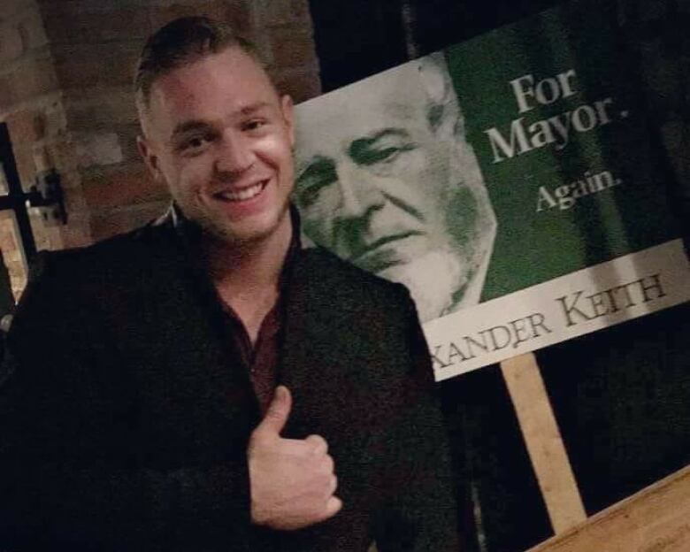 Brnadon is posing in front of an Alexander Keith's sign. 