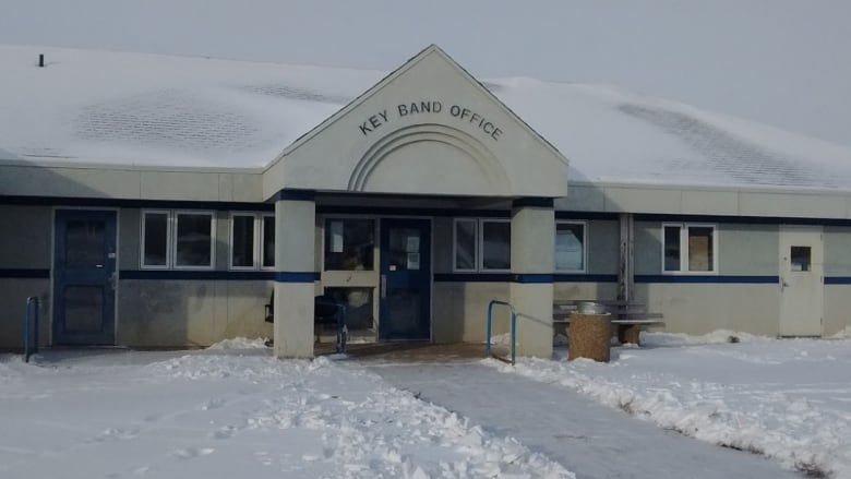 Snow surrounds a one-story government building with glass doors and several windows. Above the entryway reads, 'Key Band Office.'