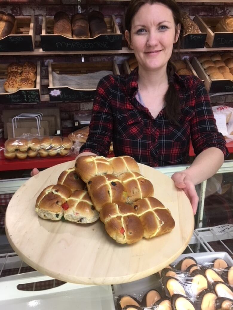 a woman holds a tray of hot cross buns