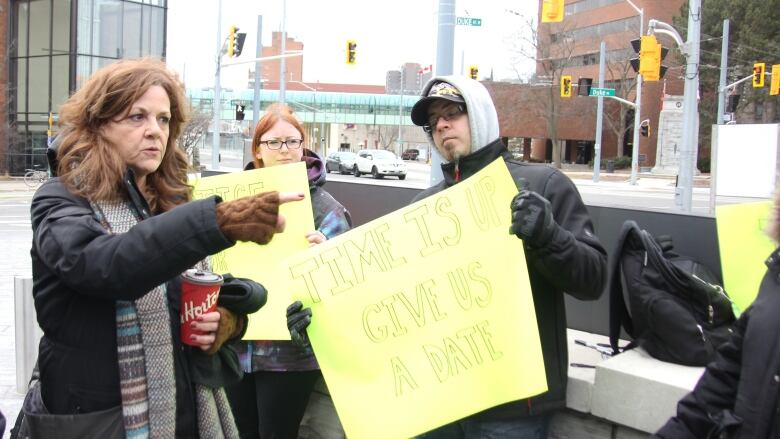 People hold yellow signs in protest - one sign reads 