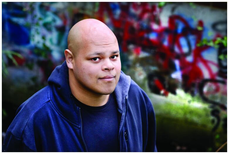 A man poses for the camera in front of a garden.