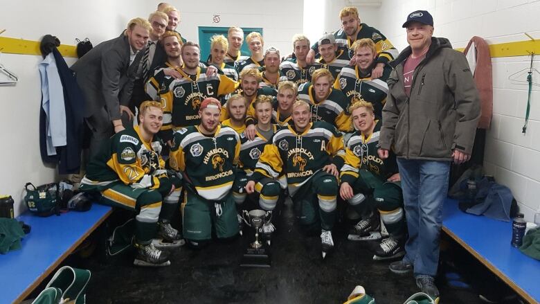 A team of hockey players and coaches huddle together for a photo.