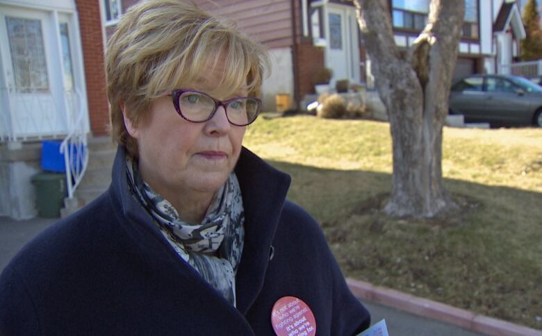 Woman with dark coat and glasses stands outside.