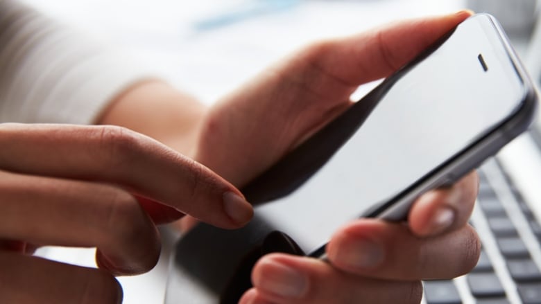 Person holding cell phone over a keyboard.