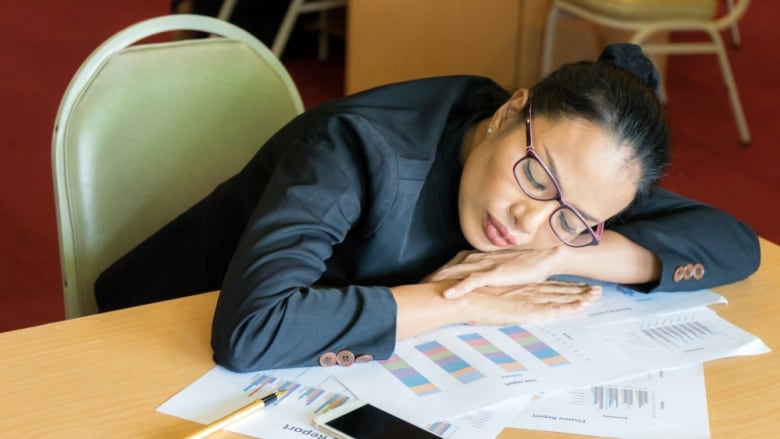 A woman with glasses sleeps at her desk.