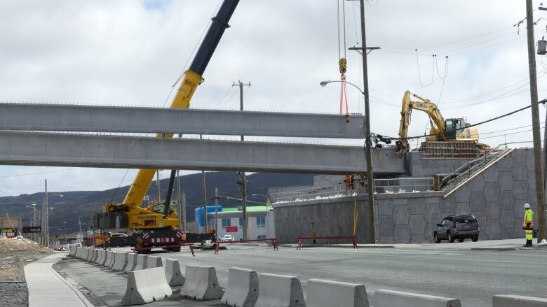 A crane lifts a concrete span into place at an overpass above Topsail Road.