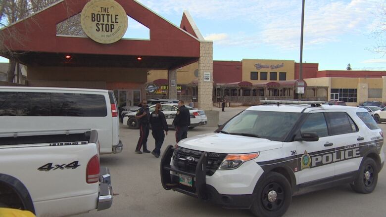 Police officers stand in a parking lot outside a business.