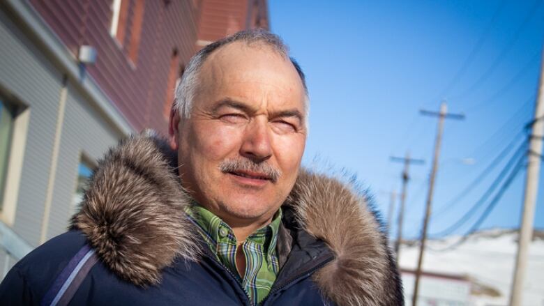 A man wearing a collared shirt and a parka squints in the sun as he looks off to the side. 