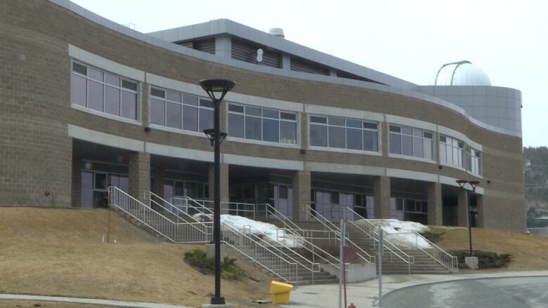 A grew building sitting above a grassy hill with stairs in the middle. 