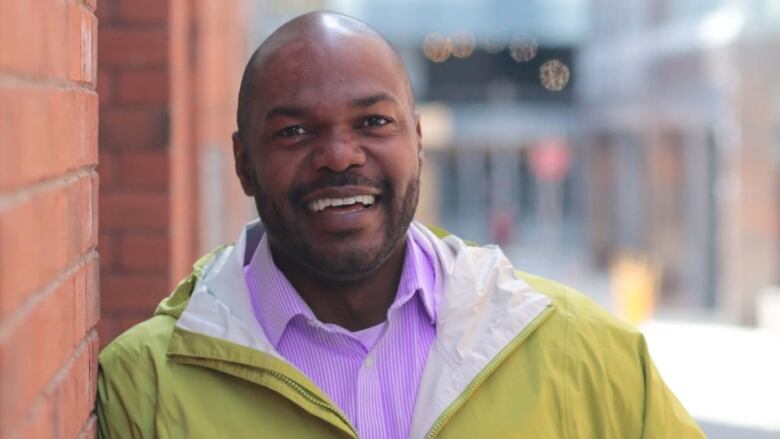 Moise is shown smiling, leaning on a brick wall.