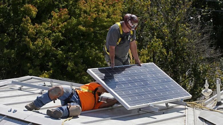 Two construction workers are shown on top of a home installing a solar panel.