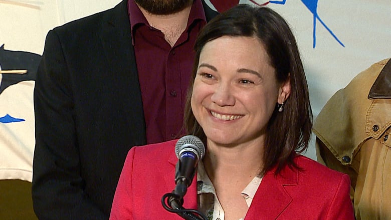 a woman in red jacket smiles at a microphone