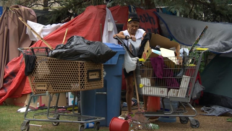 A woman sifts through items in one of two shopping carts sitting in front of tents