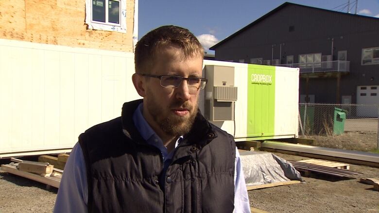 A man in glasses in front off a home under construction.