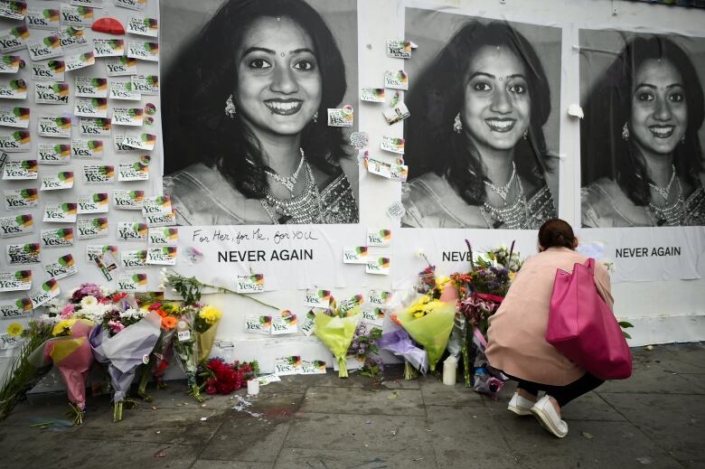 A woman places flowers in front of posters that say 