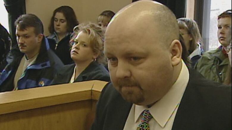 A man in black suit sitting in a court room. 