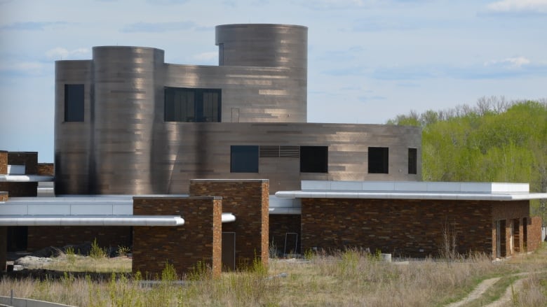 A large silver and round house is surrounded by tall grass