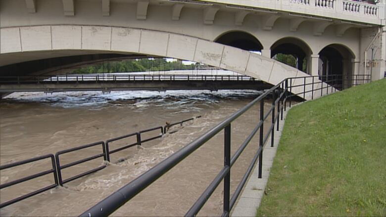 High water flows under a bridge in Calgary, flooding sidewalks