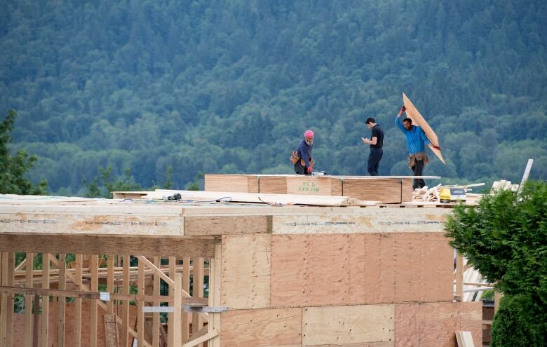 Three construction workers build a house using plywood under the shadow of B.C.'s North Shore mountains.