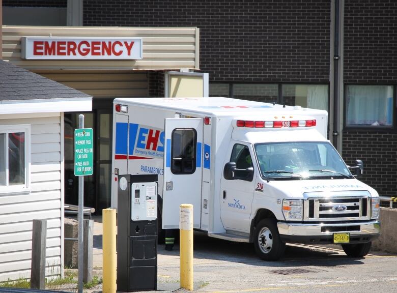 An ambulance is backed up to the door of a brick building with a sign saying 