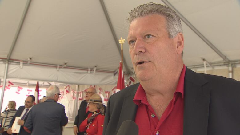 A white man wearing a red shirt speaks to a reporter off-screen.