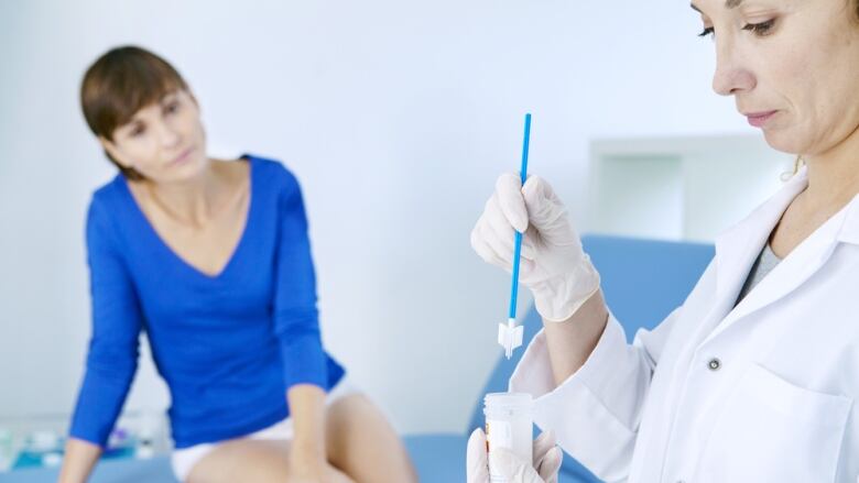 A female patient sits on a medical bed as a doctor prepares a swab. 