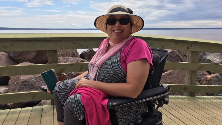 A woman wearing a hat and sunglasses sits in a wheelchair outside.