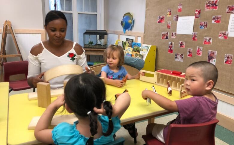 A Black adult woman supervises toddlers at a table in a child-care centre.