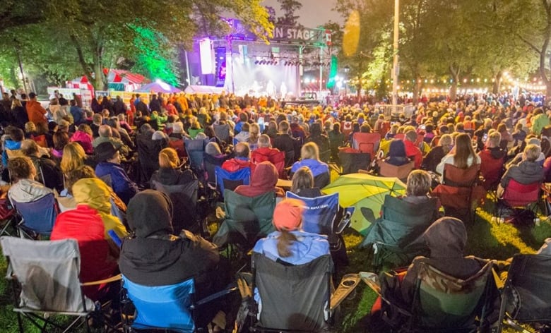 Dozens of people sitting in lawn chairs wearing rain coats looking towards a stage.