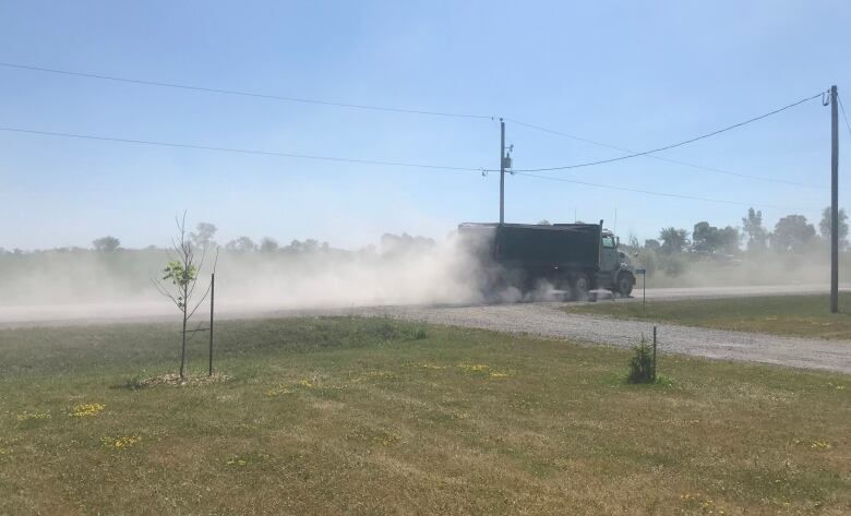 A construction truck kicks up dirt while driving on a rural road.