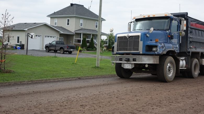 A large truck on a gravel road in front of a home.