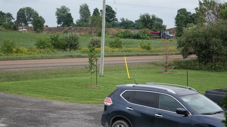 A rural road with a large pile of dirt in the background and a minivan in the foreground.