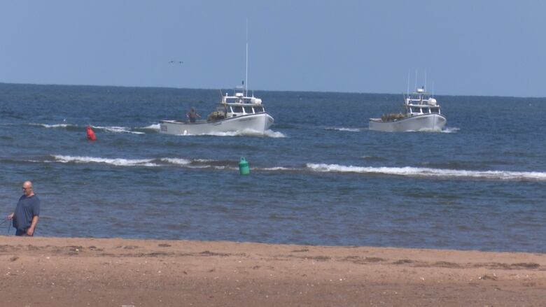 Two boats steaming past buoys near the beach at Malpeque. 