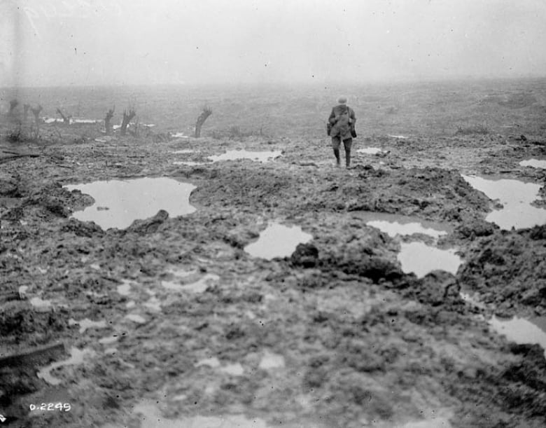 A man stands in a muddy and cratered field.