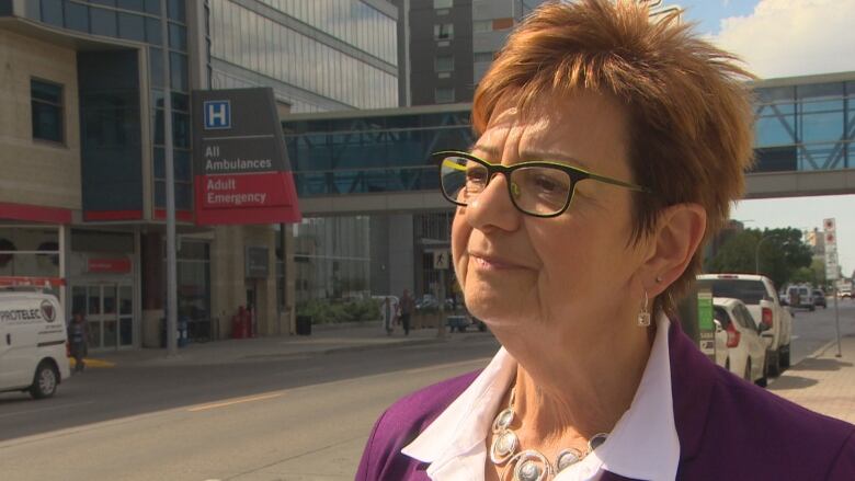 A woman with glasses and short red hair is seen in a profile outside on a street