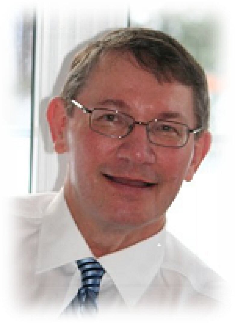 A photo of a man with glasses wearing a white collared shirt and a tie.