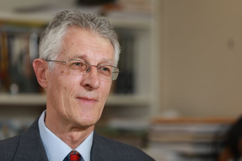 A man with grey and white hair wearing a grey suit with a red tie and glasses