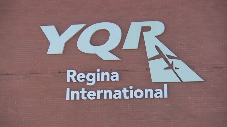 A silver sign with the Regina International Airport's logo is pinned to a brick wall.