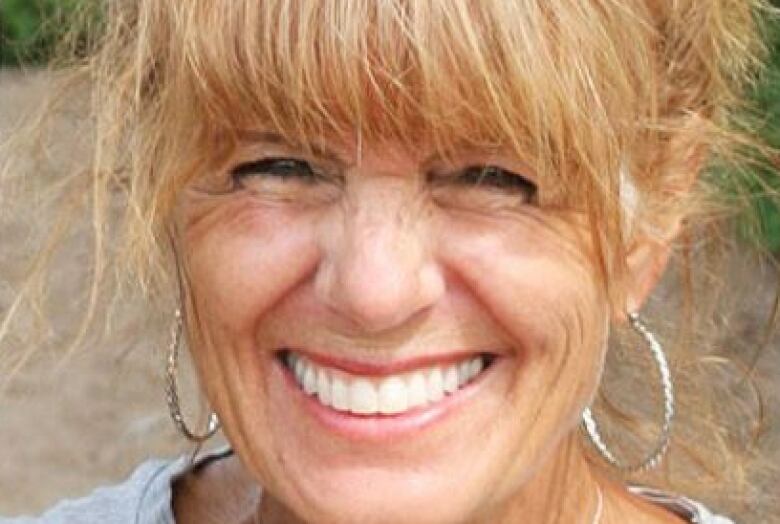 smiling woman with strawberry blonde hair tied up and silver hoop earrings