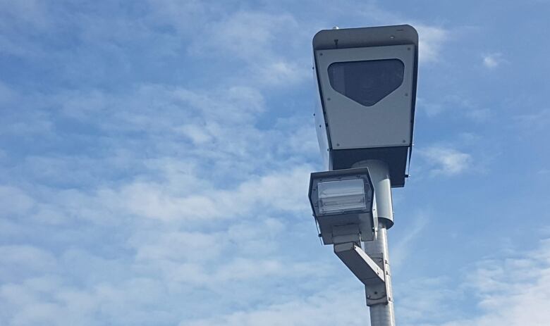 A boxy speed camera. Blue sky with some clouds in the background. 