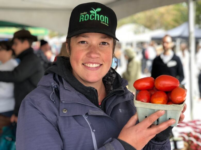 A woman stands holding a basket of tomatoes 