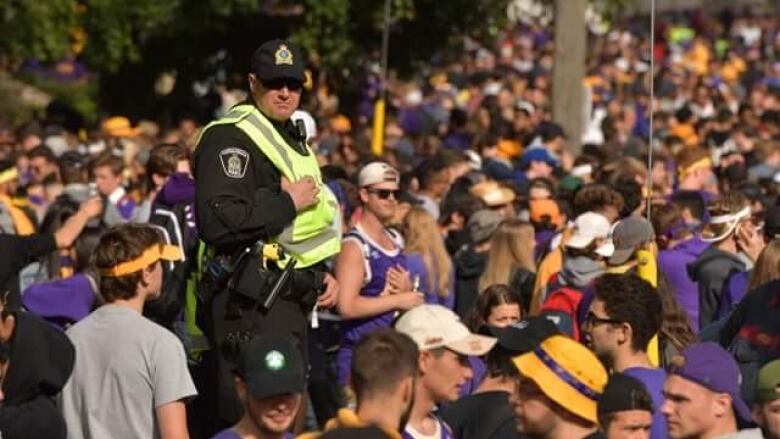 A police officer stands above a crowd of young partygoers wearing purple and yellow - the colours for Wilfrid Laurier University's athletics teams