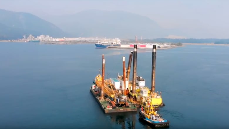 A large ship approaches a port in the distance with moutains behind.